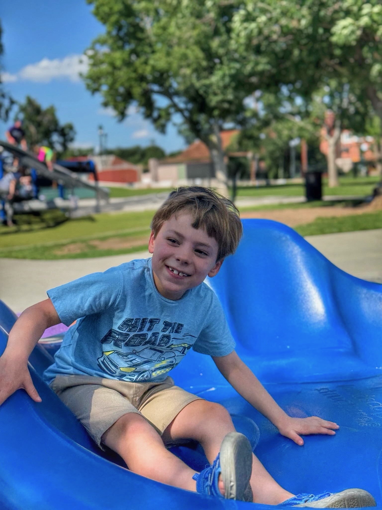 Noah grinning at the bottom of a playground slide