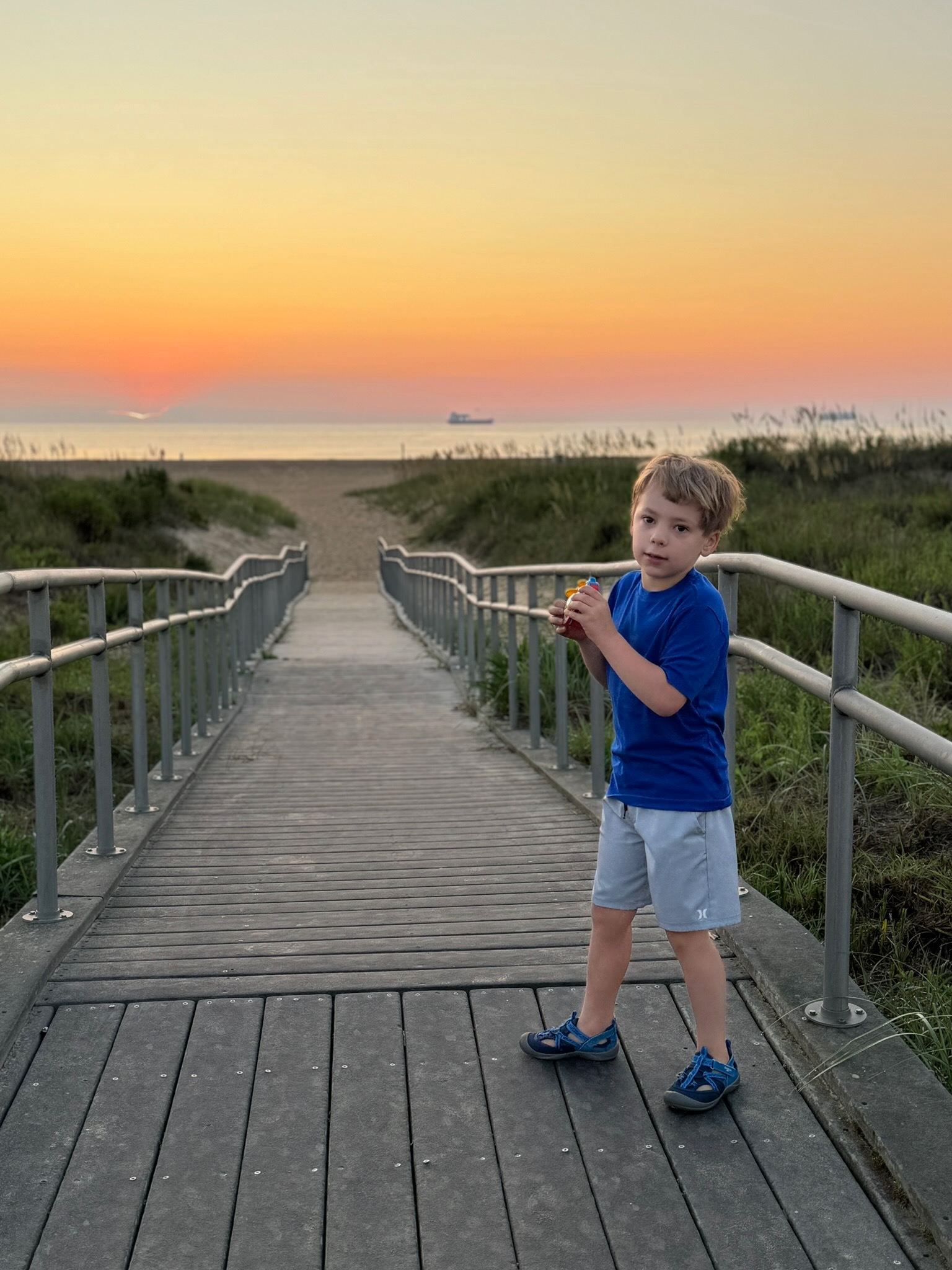 Noah at the end of the dune boardwalk, ocean and sunset behind him