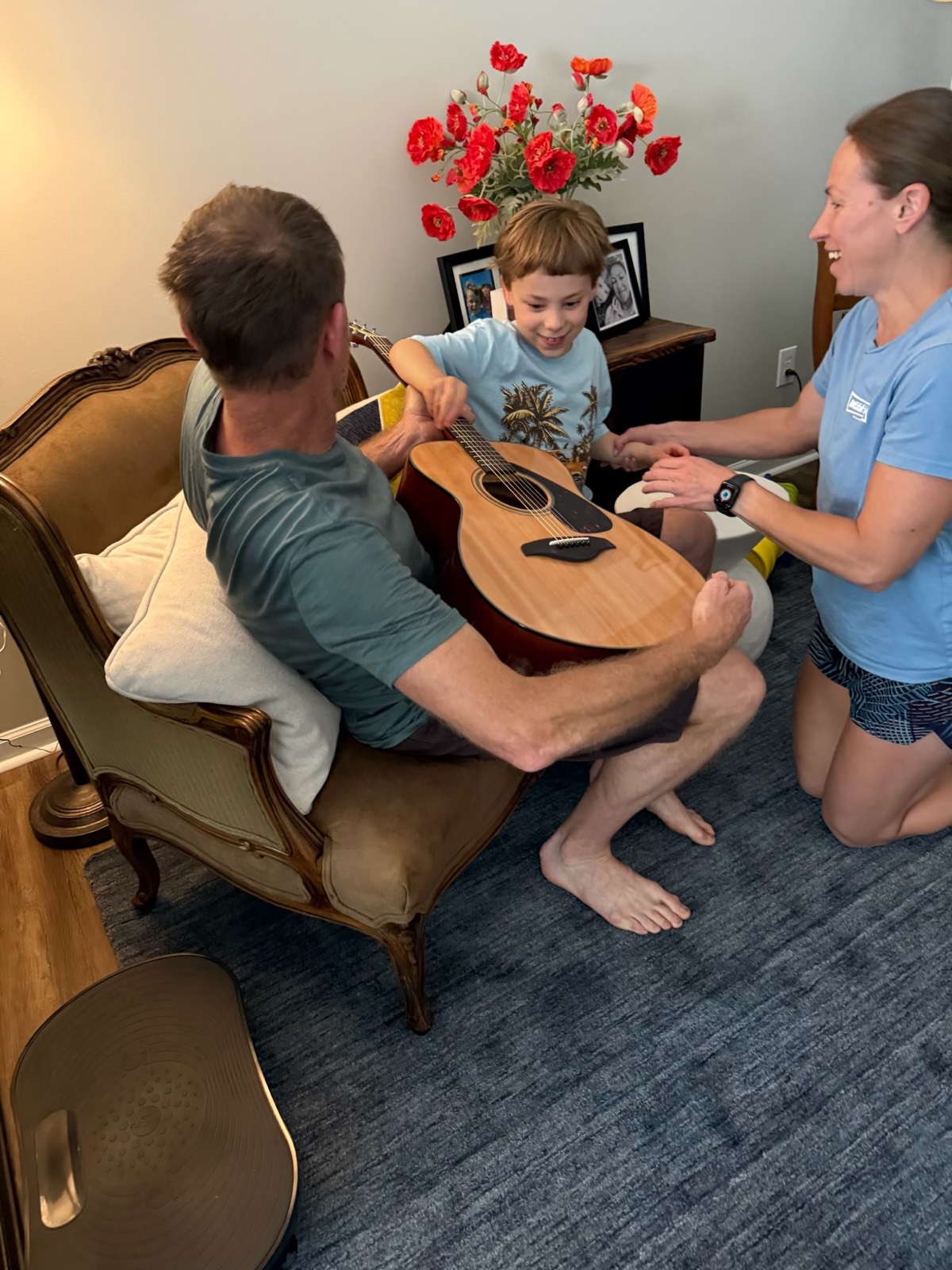Noah exploring an acoustic guitar with his dad while his mom kneels beside them